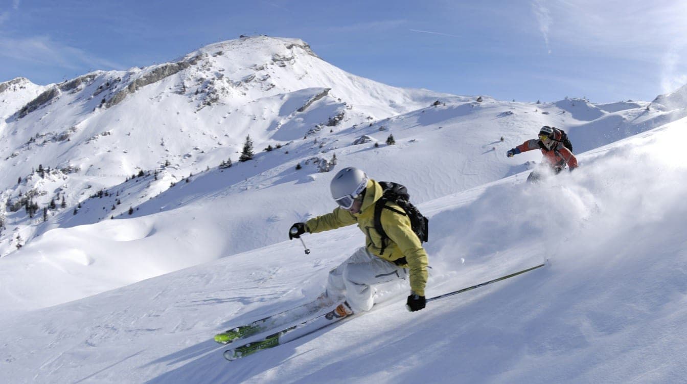 Alpine skiers carving powder below a snowy ridge