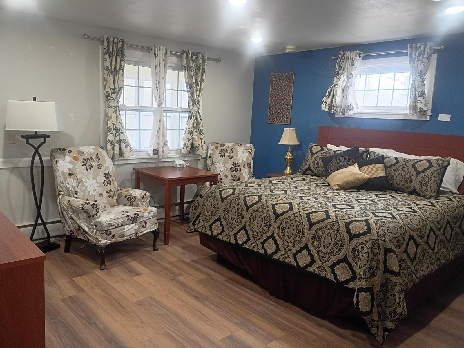 King bed with medallion-pattern bedding, floral wingback chairs and bright windows